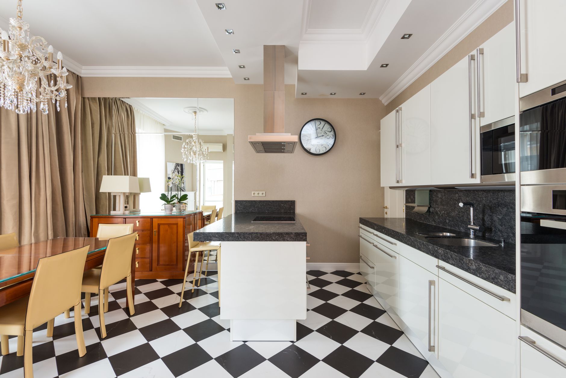 Interior of modern kitchen with marble counter and built in appliances with chairs at wooden dining table in Riverside, CA